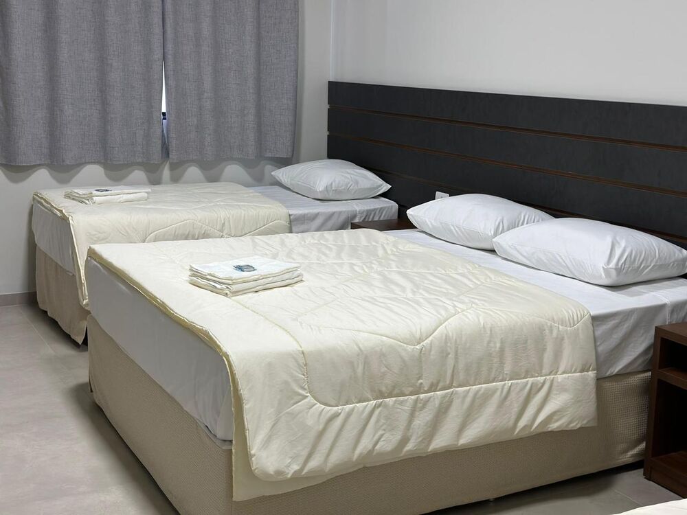 Quarto com cama de casal e cama de solteiro, toalhas dobradas sobre o edredom